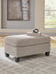 Beige upholstered ottoman on a patterned rug beside living room furniture